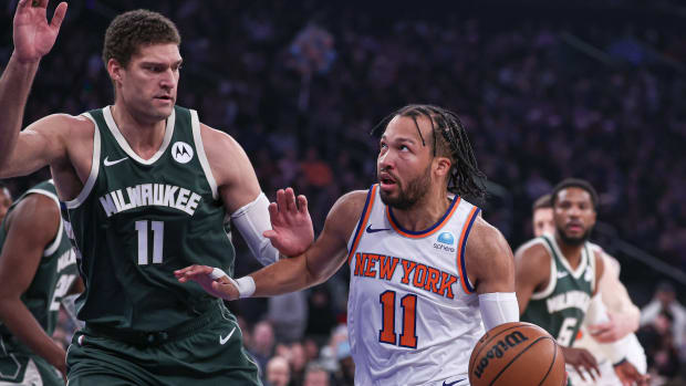 Jalen Brunson looks up toward the basket as he dribbles with one hand and is guarded by a Bucks player